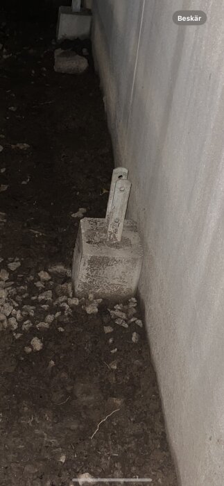 Grå betongpelare står på marken vid en vägg i dunkelt ljus.