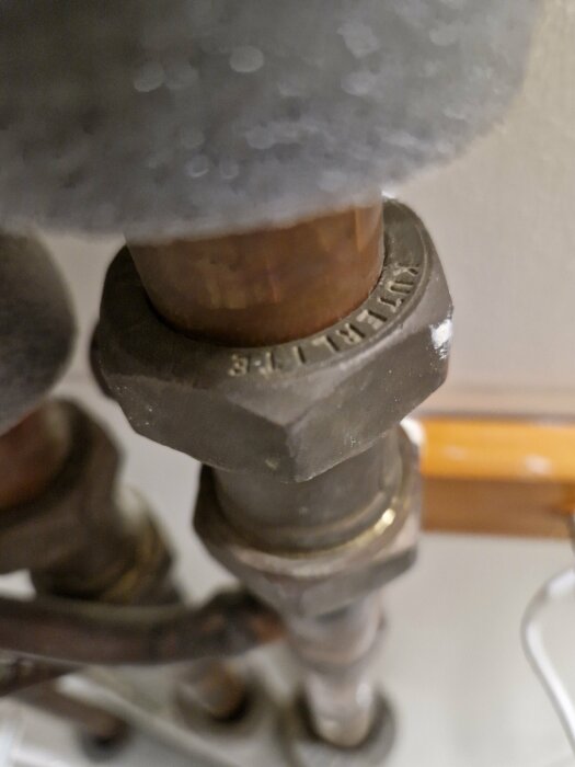 Närbild på rostigt rör och ventil, möjligen del av värme- eller vatteninstallation, med skruvade kopplingar.