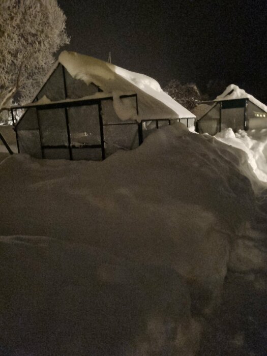 Ett hus och staket täckta av tjocka lager snö på natten.