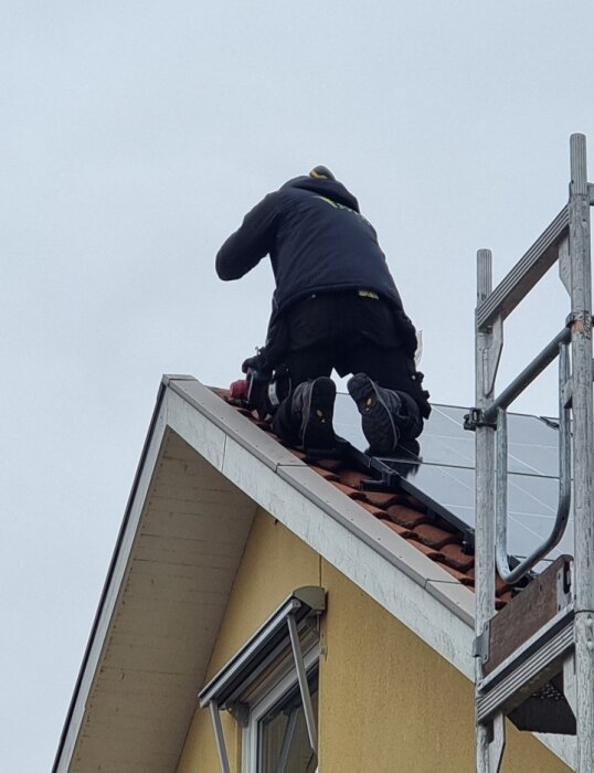 Person i arbetskläder arbetar på ett hus tak vid sidan av en byggställning.