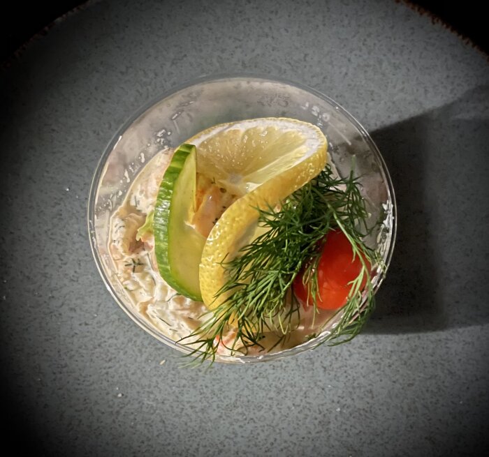 Ett glas med skaldjursröra, garnerat med citron, dill, gurka och tomat.