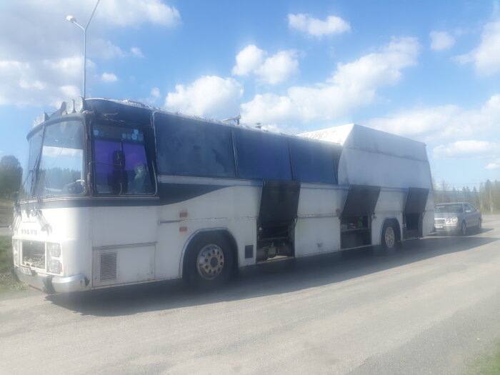 En vit ombyggd buss med öppna förvaringsfack parkerad vid en väg på dagen.