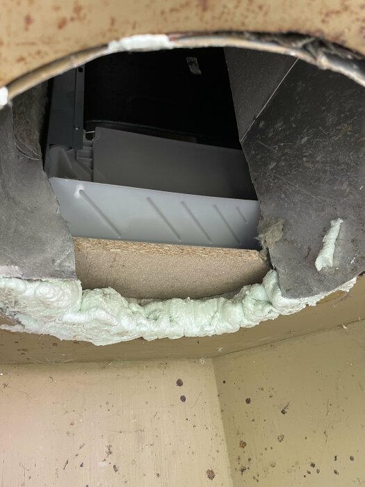 Utsikt genom ett hål i väggen, isolering syns, inre strukturer av byggnadsexponering.