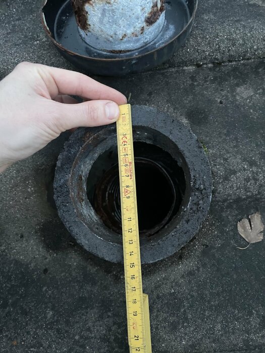 Mätning av brunnens diameter med måttband, rostig kant, utomhus, dagtid, asfaltbakgrund.