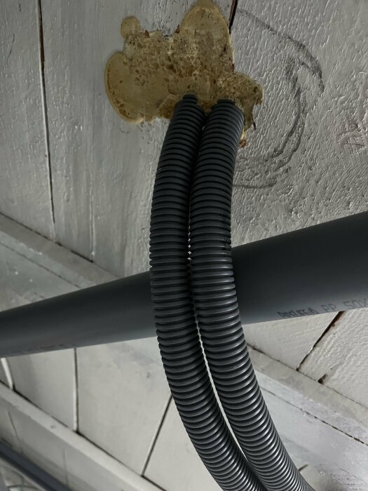 Två svarta flexibla rör genom skumexpansion vid vitt tak. Installationsdetalj, konstruktion, byggnad teknisk lösning.