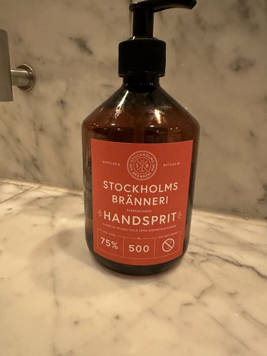 Brun handdesinfektionsmedel med pump på marmorbänk. "Stockholms Bränneri Handsprit", 500 ml, 75% alkohol.