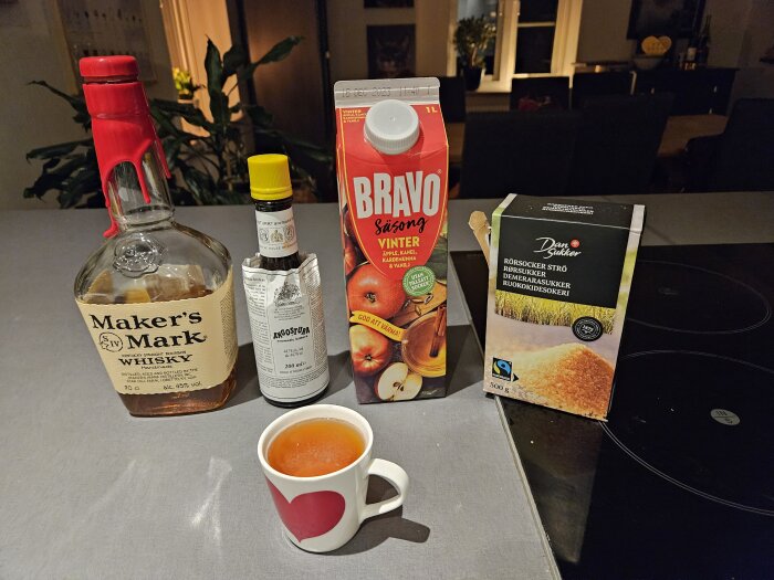 Whiskyflaska, bitter, juice, rörsocker, kopp på köksbänk. Möjlig cocktail-förberedelse eller bakningsaktivitet.