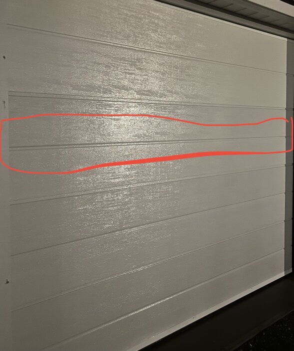 Garageport med horisontella linjer och en röd markering. Skumringsbelysning, delvis skuggat.