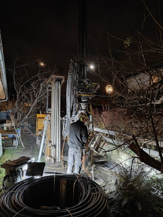 Arbetsplats nattetid, borrningsutrustning, arbetare i säkerhetskläder, elektriska kablar, industriell miljö, utomhus, konstgjort ljus.