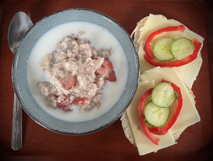 Havregrynsgröt med rött bär, mackor med ost, gurka och paprika, frukost, sked, träbord.