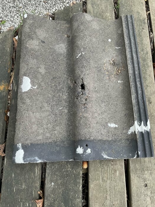 Äldre bitumen takmaterial ligger på träplankor med synlig slitage och ett hål.
