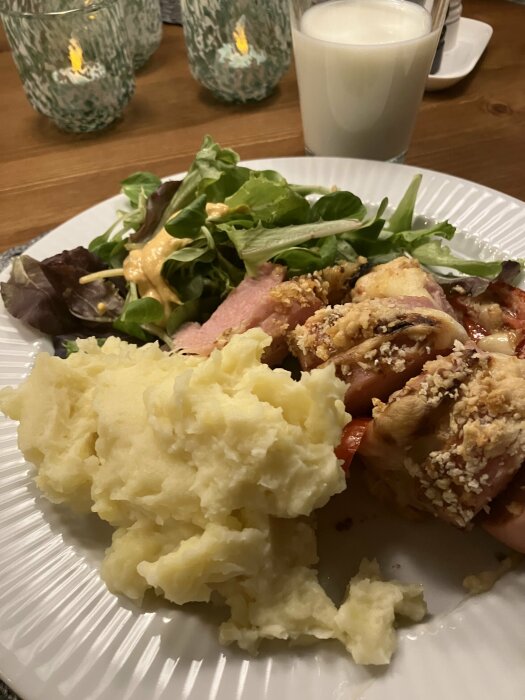 Middag med potatismos, kyckling, sallad, sås och ett glas mjölk. Två levande ljus i bakgrunden.