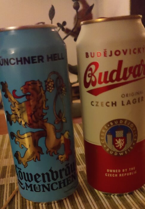 Två ölburkar, en Löwenbräu och en Budvar, med emblem, på ett bord.