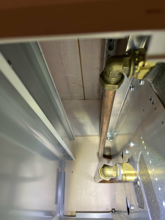 Bild inifrån uppochned av ett metallfäste och kopparrör, möjligtvis del av en apparat eller maskin.