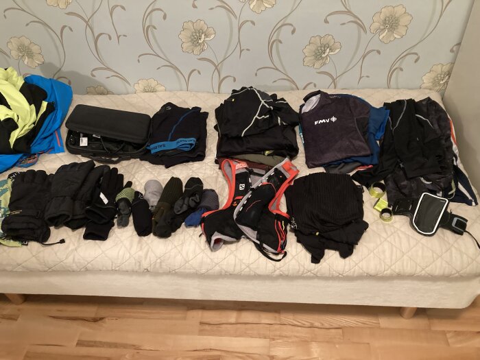 Sportkläder och utrustning ordnade på en säng, inkluderar handskar, strumpor och mobilhållare.