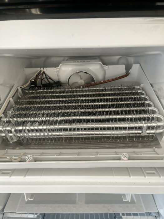 Kylskåpets inre med avfrostad, isfri förångare och fläkt. Tekniska komponenter synliga, ingen matlagring.