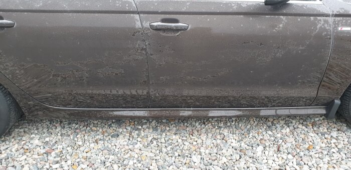 En smutsig bil dörr och panel med stänk, på en grusig yta.