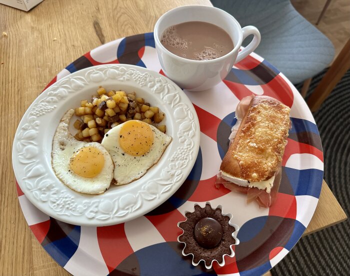 Frukostdukning med ägg, potatis, smörgås, chokladpralin och varm kakaodryck på brittiskt temad bordstablett.