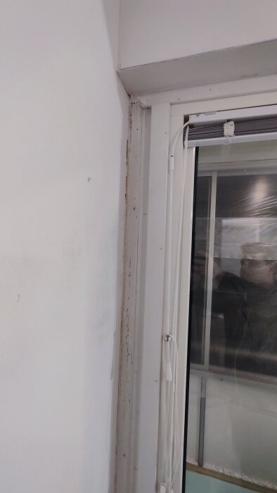 Hörn av ett rum med fönster, vita väggar, skador och smutsstrimmor vid list och vägg.