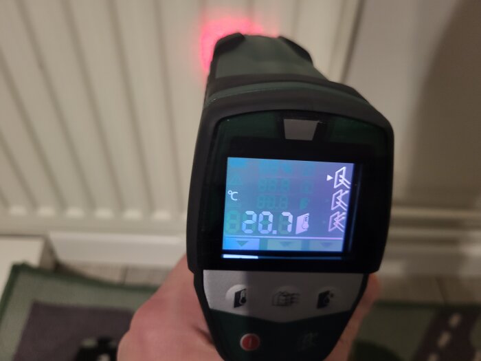 En handhållen infraröd termometer visar en temperatur av 20.9 grader Celsius framför en radiator.