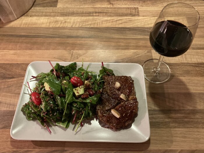 Middag med grillad biff, sallad, quinoa, tomater, och ett glas rött vin.