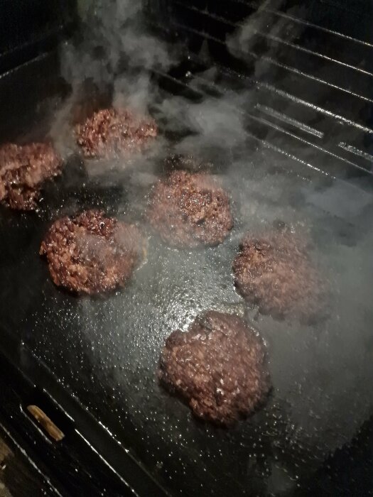 Hamburgare steks på grillpanna, rykande och brunande, matlagningsprocess i köket.