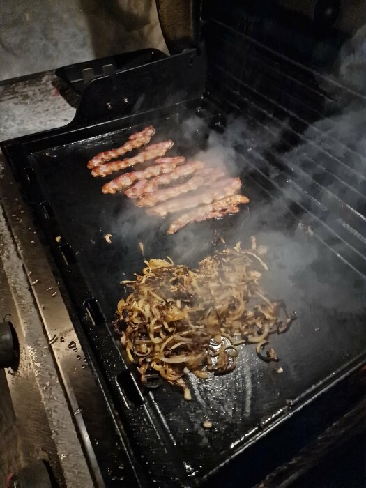 Fläskbacon och lökar grillas på en BBQ-grill; mycket rök och ånga syns.