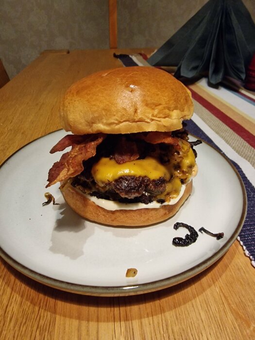 Dubbel cheeseburgare med bacon på ett vitt fat, majonnäs, smält ost, hemmiljö.