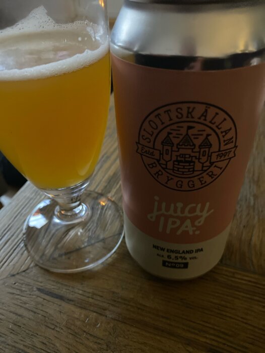 En burk Juicy IPA-öl från Slottskällans Bryggeri bredvid ett glas med öl.