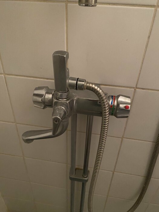Kromad duschblandare med justeringshandtag på kakelvägg, duschslang ansluten, temperaturmärken synliga.