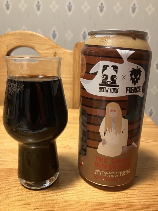 En mörk öl i ett glas bredvid en burk med etikett "The Ghost Dimension" av Brew York & Fierce, 12% alkoholhalt.