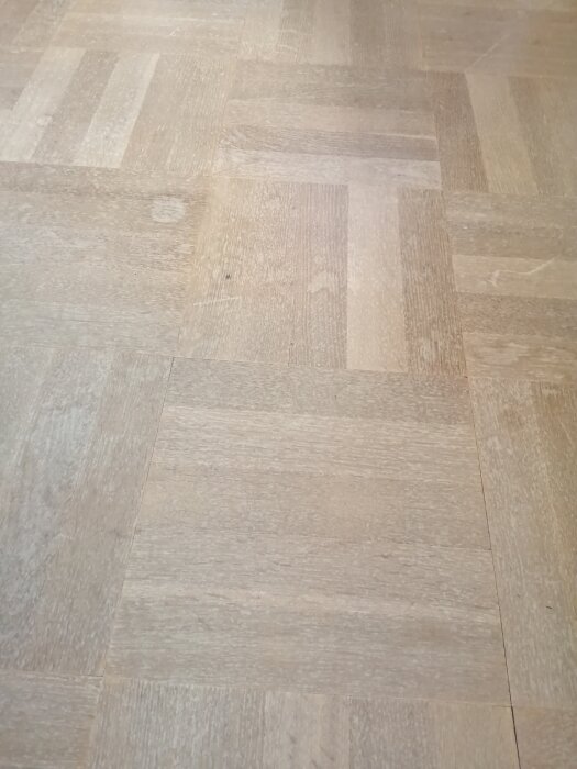 Ljust trägolv med rektangulära parkettbitar i varierade nyanser av beige och brunt.