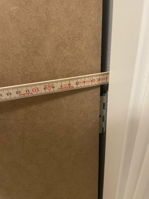 Måttband mot en dörrkarm i en inomhusmiljö för att mäta bredd.