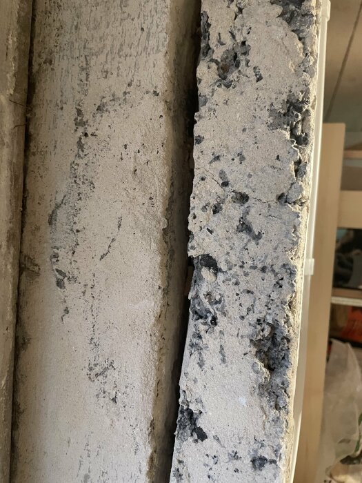 Grovt betongyta nära en slät vägg, detaljer i byggmaterial med ojämn textur.