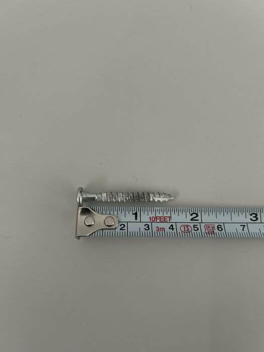 Skruvi, jonka vieressä on mittanauha. Skruvin pituus on noin 5 cm.