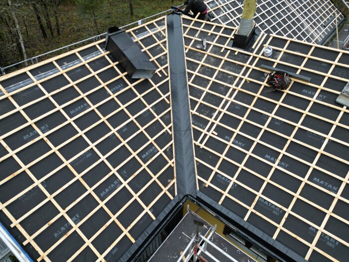 Tak under konstruktion med vattentätt membran och träreglar, verktyg syns, potentiellt för takläggning.