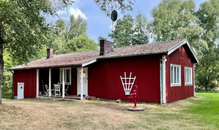 Ett rött hus med vita knutar, gräsplätt, träd, fönsterluckor, veranda och en frisbeegolfkorg.