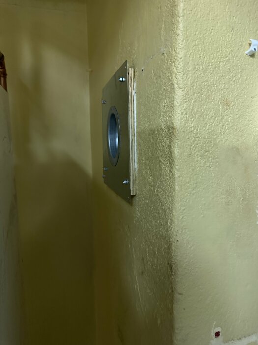Metallucka på gulfärgad vägg, troligtvis en tvättstugebokningstavla, delvis öppen och tom, med synlig låsanordning.