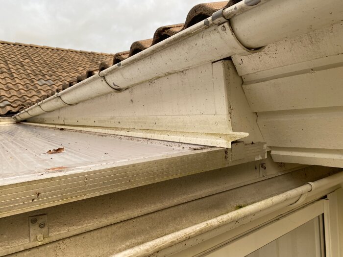 En närbild på takrännor och takpannor på ett hus med synlig tätning och lite skräp.