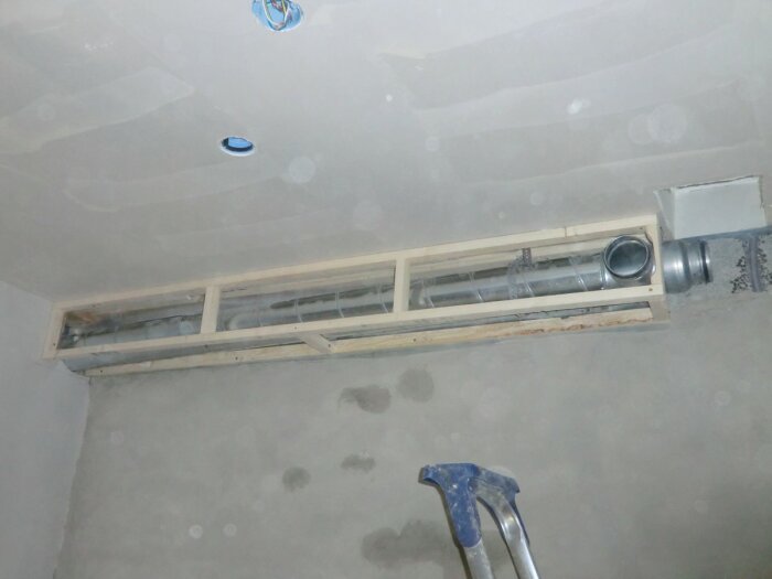 Upplyst, oavslutat ventilationsschakt med träram, ventilationsrör, delvis putsad vägg och stege.