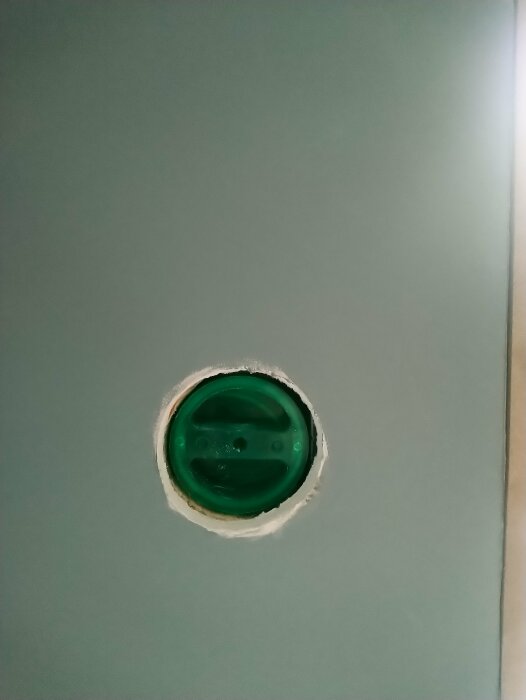 Ett hål i väggen med en grön plastkåpa synlig genom öppningen.