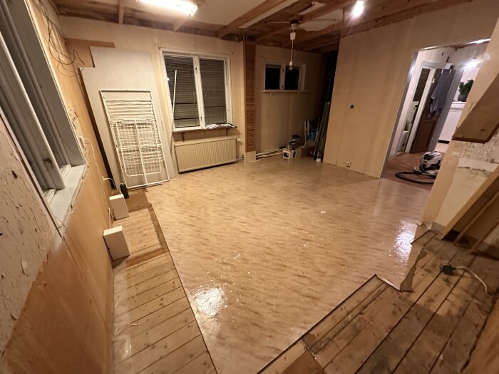Ett tomt rum under renovering med trägolv, oskyddade väggar och renoveringsmaterial utspritt.