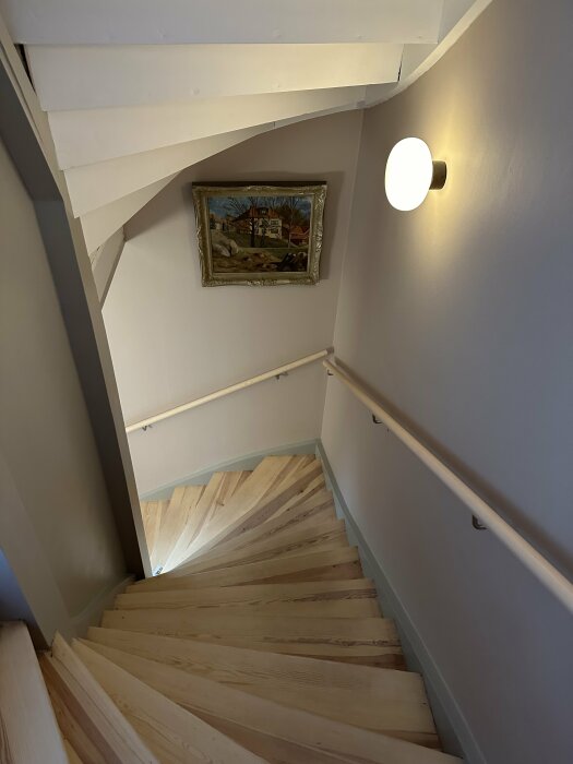 Bild på trapphus med trätrappor, vit vägg, konsttavla och en rund vägglampa.