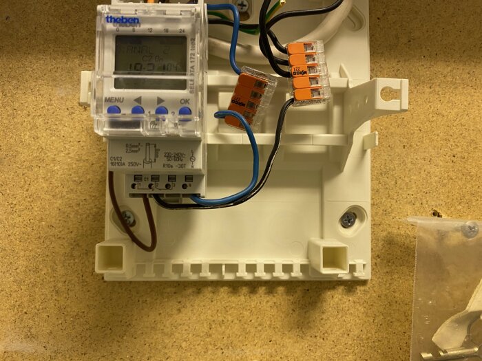 Digital timer med LCD-display monterad på vägg, ansluten med elektriska kablar och kopplingsklämmor, installationsarbete pågår.