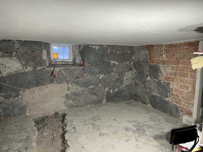 Källarutrymme under renovering med sten- och tegelväggar, litet fönster, osynliga tak och golv.