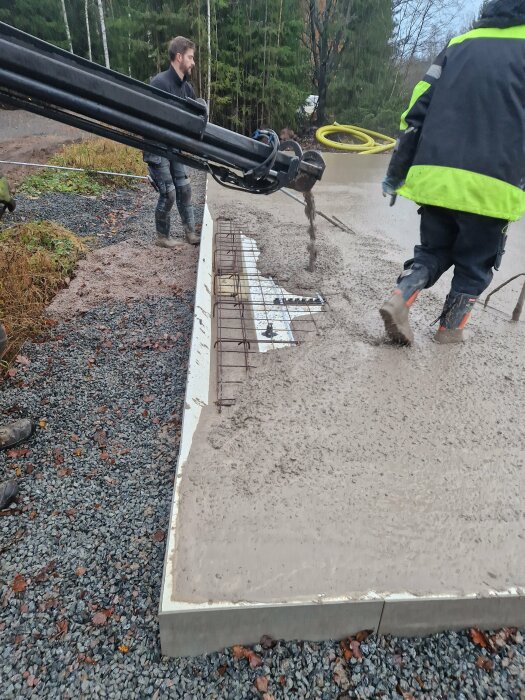 Arbetare häller betong för grundläggning med hjälp av betongpump. Byggarbetsplats, grå dag.