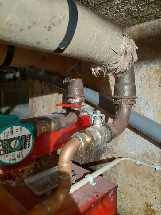 VVS-installation med isolerade rör, ventiler och cirkulationspump i en krypgrund eller källare.