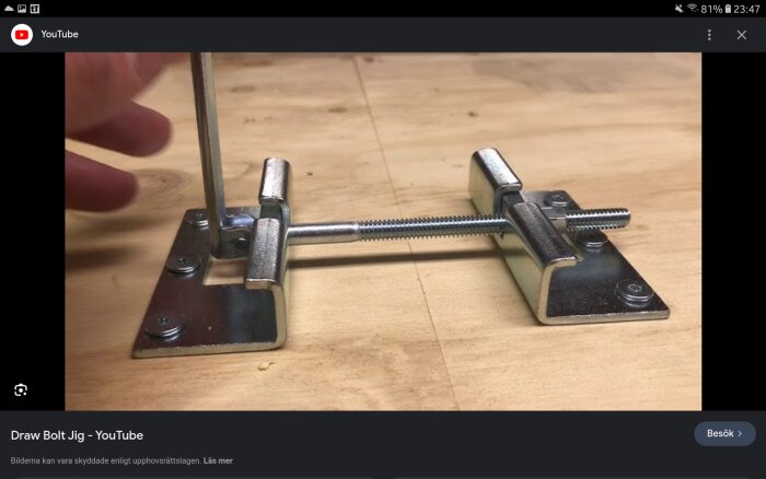 Metallverktyg för spänning med skruv och vingmuttrar på träyta, troligen en länkbultsmall.