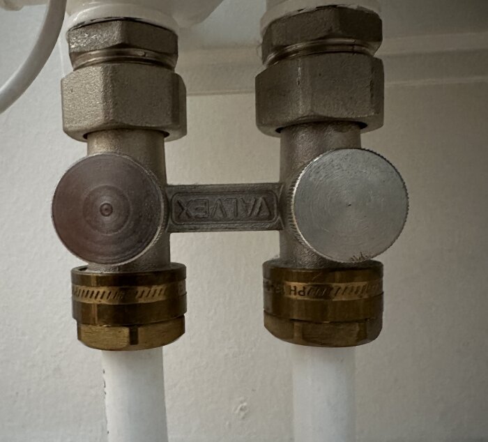 Två vita rör med mässingskopplingar och vred anslutna till en VALTEC-radiatorfördelare.