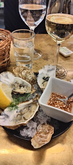 Skaldjursförrätt med ostron, citron, sås och brödkorg, serverat med vitt vin och vatten.
